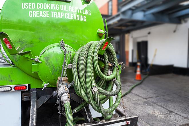 a professional plumber using a pump to empty a grease trap in Burbank